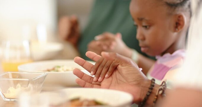 African American mother guiding daughter pressing palms at table for prayer with bowls, copy space