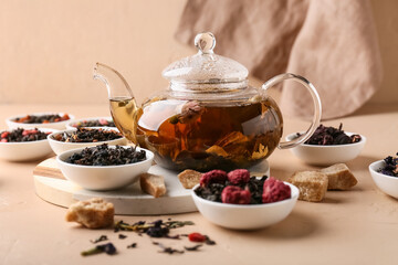 Bowls with dry fruit tea and teapot on beige grunge background, closeup