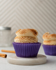 Close-up of a vanilla cupcake in a purple wrapper topped with swirled buttercream frosting and cinnamon dust, Vanilla cupcake with piped buttercream frosting in a purple liner