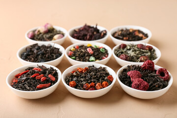 Bowls with different dry fruit tea on beige grunge background, closeup