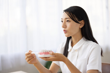 Woman in white coat demonstrating tooth brushing with dental model