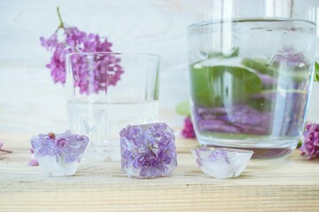  Lilac flowers, ice cubes and a glass of water on a light background and lilac flowers in a vase