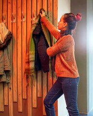 Young woman in sweater and jeans putting on jacket in warmly lit hallway of coffee shop