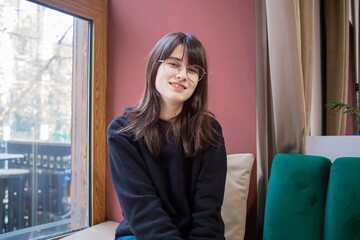 Smiling young woman wearing glasses posing by the window