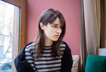 Pensive and worried young woman near the window in soft natural light
