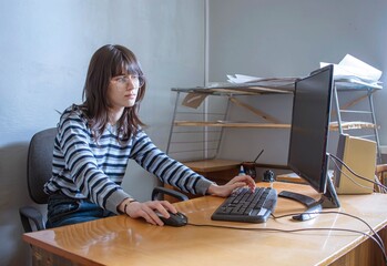 Young woman wearing glasses turns on computer at her desk