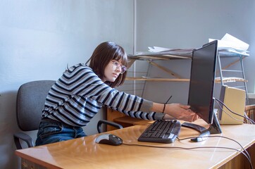 Young woman wearing glasses turns on computer at her desk