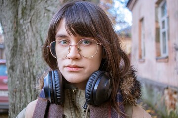 Pensive young woman with headphones and glasses outdoors