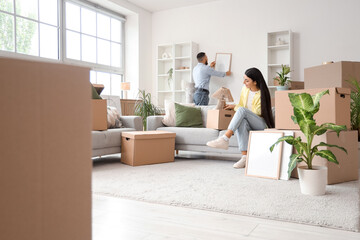 Happy young couple hanging frame in rented apartment on moving day