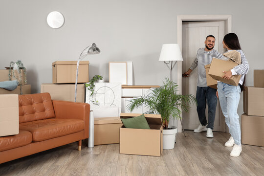 Young couple with boxes entering through door into rented apartment on moving day