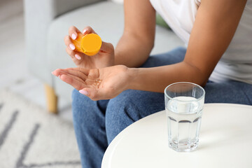 Young woman taking vitamin E pill at home, closeup