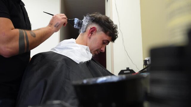 Professional barber carefully applying bleach and oxidant mix using comb and spatula
