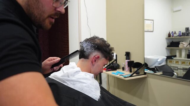 Professional barber spreads mixed bleach and oxidant cream on client&rsquo;s hair to lighten tone