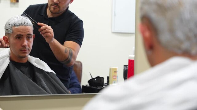 Customer raises head to look at bleaching progress as hairdresser works and another waits behind