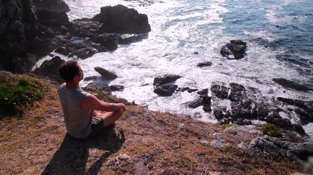 Man sitting at vantage point overlooking ocean doing deep breathing meditation