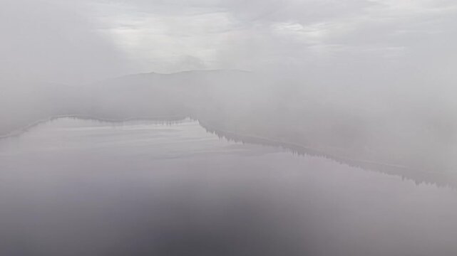 silent grey fog enveloping hidden lake with muted tones, aerial approach through low visibility, subtle
