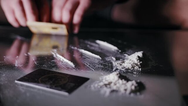 Moody low light reveals white powder prop on table, subtle hand motion nearby