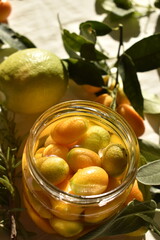 Preserved kumquats in sugar syrup in a jar decorated with fresh herbs