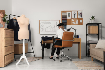 Female tailor sewing clothes at table and mannequin in atelier, back view