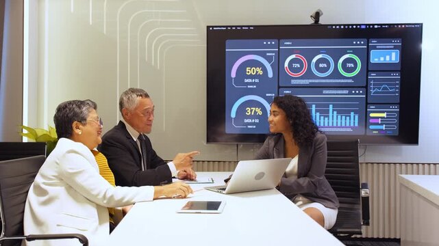 An Indian female presenter shares sales statistics and strategic insights on a large screen with Asian senior clients during a corporate seminar, fostering collaboration and professional planning.