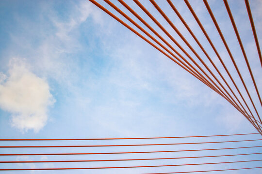Abstract view of bright orange bridge cables stretching across the sky, creating clean geometric lines and a minimalist architectural composition