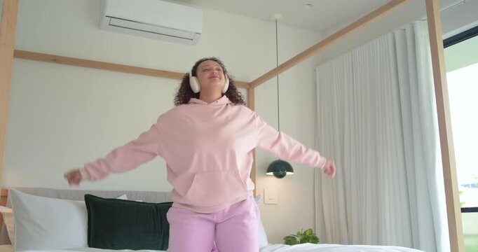 Music starting adult woman standing on bed dancing hopping grabbing phone and singing to match beat