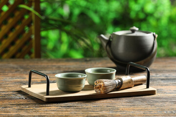 Tray with cups of matcha tea, chasen and teapot for ceremony on wooden table outdoors, closeup