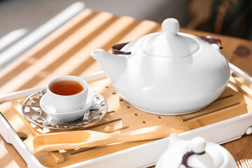 Teapot with cup of tea on wooden table in room, closeup