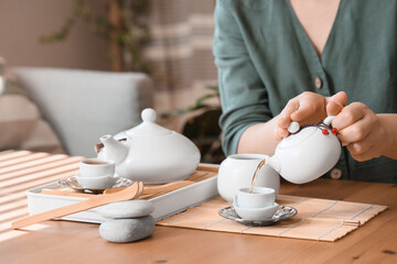 Woman pouring Asian tea into cup on table at home, closeup