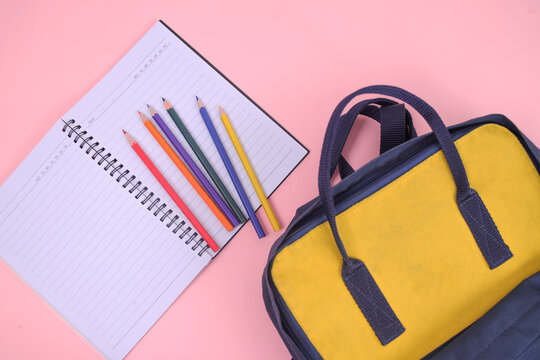 Vibrant Colored Pencils Ready for Creative Learning Next to Open Notebook and Bright Yellow Backpack