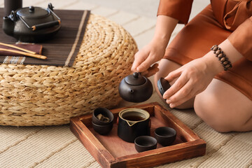 Asian woman pouring tea on carpet at home, closeup