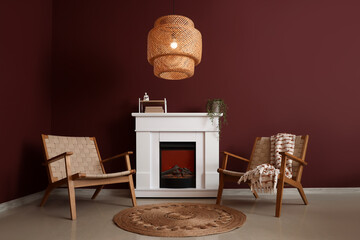 Interior of stylish living room with cozy armchairs, fireplace and glowing lamp near red wall