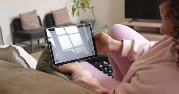 Adult woman is adjusting tablet on lap to reduce window glare while settling on couch