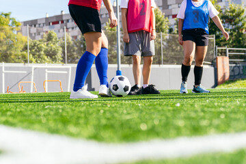 Three women footballers standing on green artificial turf with a soccer ball, preparing for practice on a sunny day