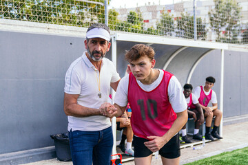 Soccer coach providing support and guidance to a young player as he enters the game from the team bench