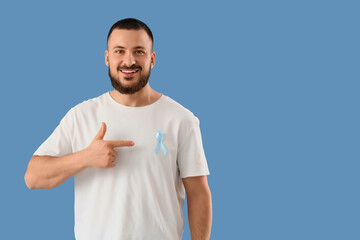 Young man pointing at blue ribbon on color background. Prostate cancer awareness concept