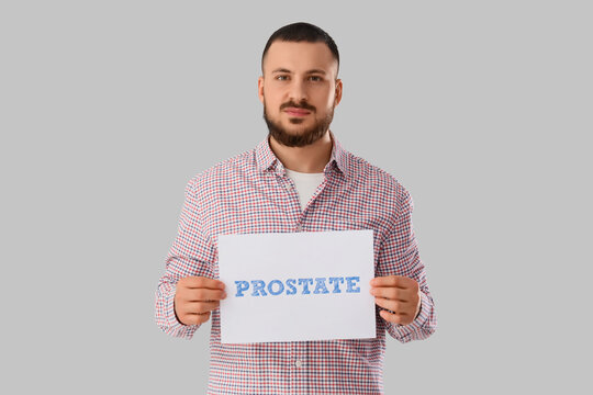 Young man holding paper with word PROSTATE on light background. Cancer awareness concept - Powered by Adobe