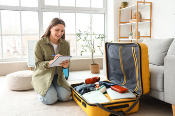 Female tourist making checklist while packing suitcase at home