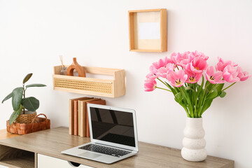 Beautiful bouquet of tulip flowers with laptop and books on table at workplace