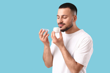 Young man sniffing cream on blue background