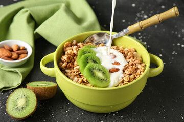 Bowl with granola, yogurt, kiwi and almonds on black speckled background