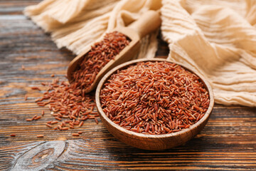 Bowl and scoop with raw brown rice on wooden background