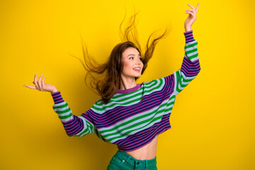 Young woman dancing in a colorful striped sweater against a yellow background celebrating joy style and fashion