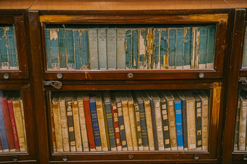 Mumbai, India Row of old worn books stored behind glass in a wooden cabinet. A vintage archival collection showing aged covers and historical literature.