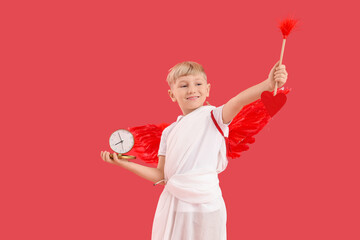 Obraz premium Cute little happy boy dressed as cupid with alarm clock and arrow on red background. Valentine's Day celebration