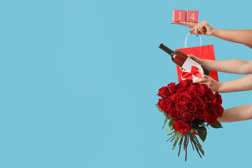 Female hands with roses, bottle of wine, gift boxes and shopping bag on blue background. Valentine's Day celebration