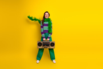 Fototapeta premium Young woman with colorful striped sweater green pants and a retro boombox stands against a bright yellow background
