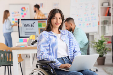 Female designer in wheelchair working with laptop at office