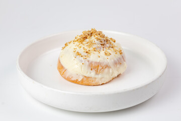 Cinnabon roll with cream cheese glaze and crumb topping on white plate against clean background.