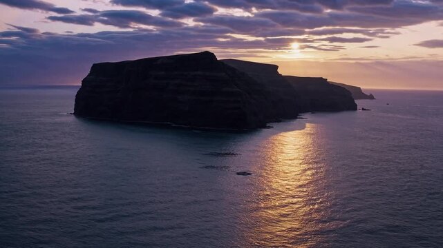 As the sun sets, a stunning orange glow reflects off the calm ocean water, creating a serene atmosphere along the rugged cliffs. Dark clouds blanket the horizon, enhancing the dram